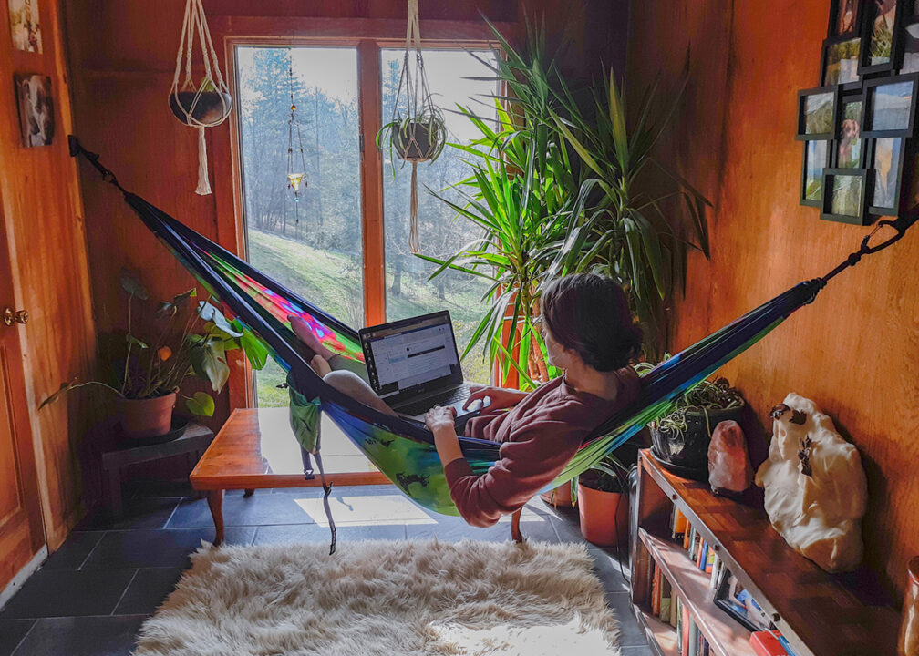 A woman sits in her Tie Dye Hammock inside her house using the Deluxe Indoor Hammock Hanging Kit.