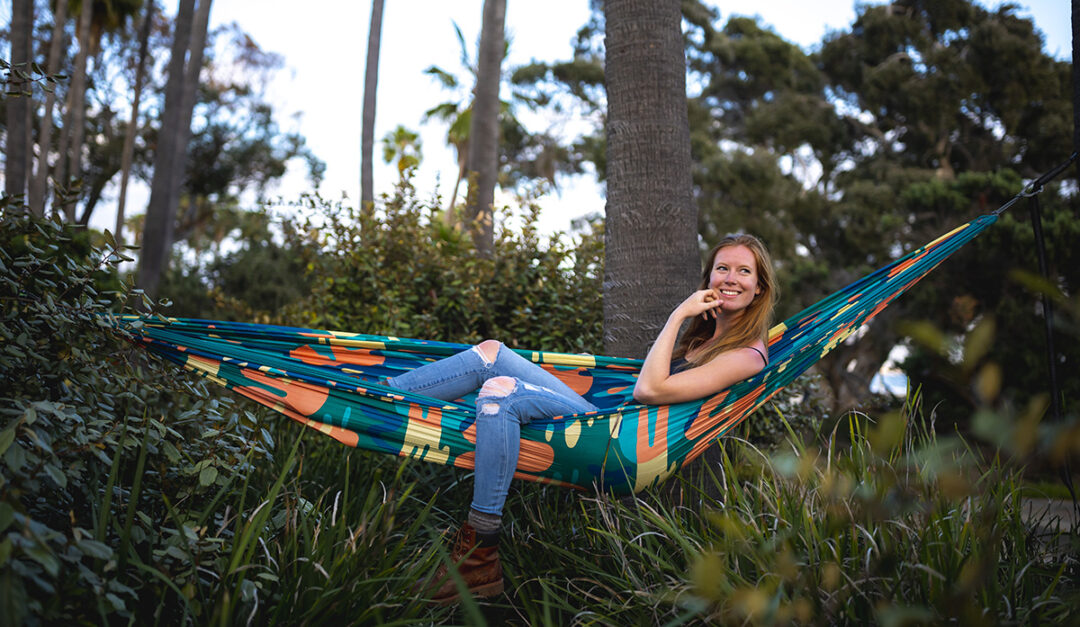 A woman lies in a colorful DoubleNest Print Hammock in the Lagoon print.
