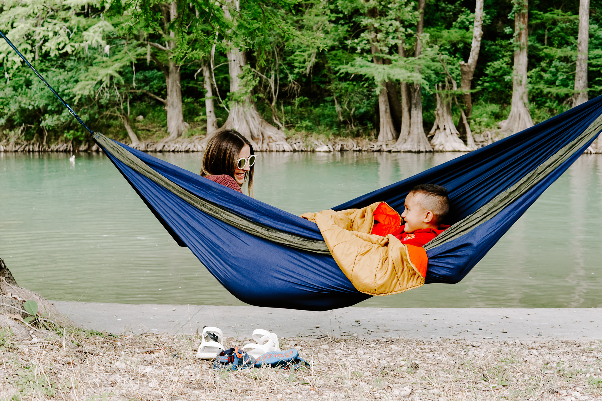 A woman and her son share a DoubleNest hammock by the water.