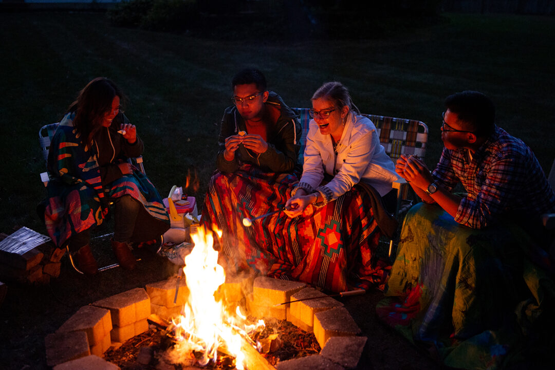 A group of four people using FieldDay Blankets roasting marshmallows by fire.