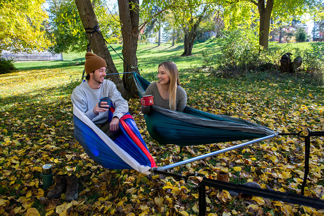 A man and woman drink coffee in side-by-side DoubleNest hammocks while using the Fuse Tandem Hammock System