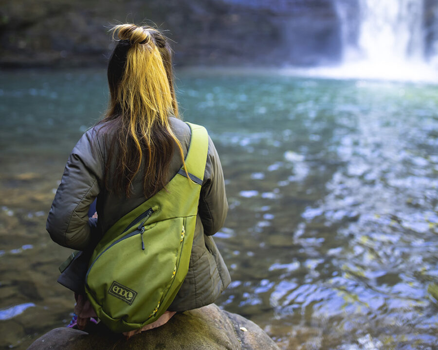 Woman wearing Kanga Sling Pack by waterfall.
