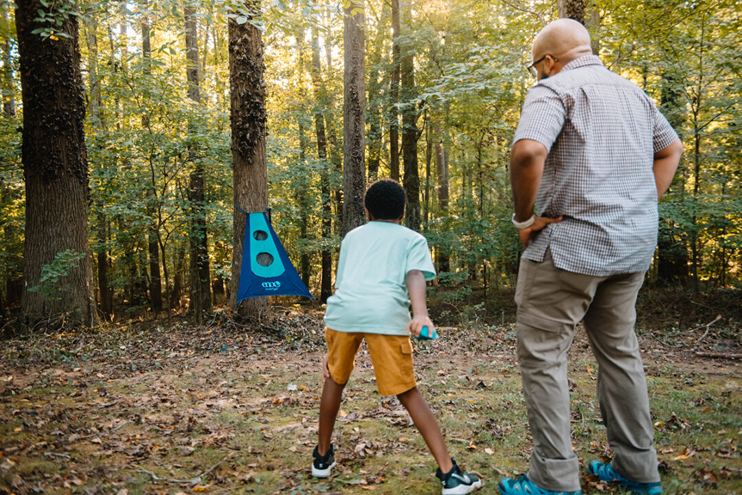A man watches as his son throws a bean bag while playing TrailFlyer Outdoor Game