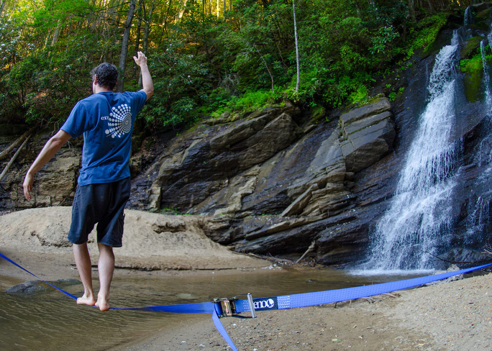 A man walks on the Slackwire Slackline near a waterfall