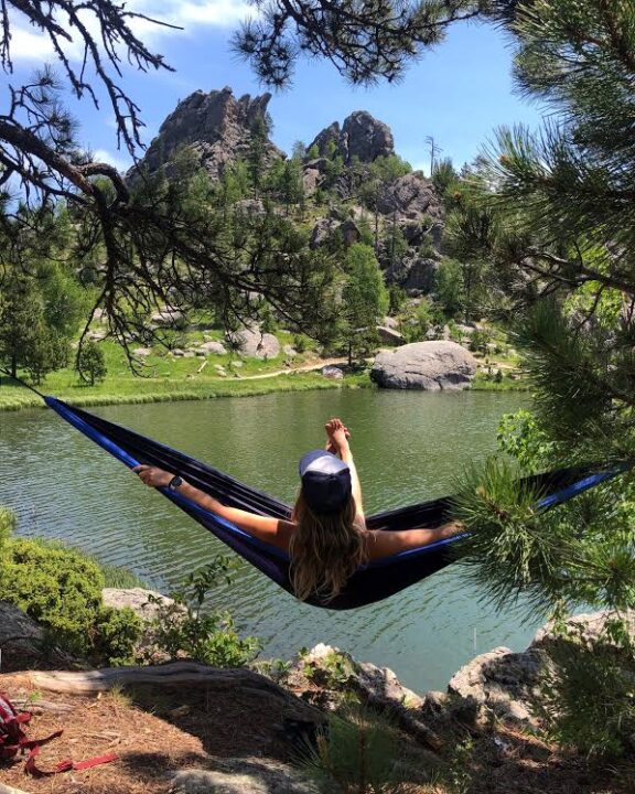 A woman sits in her hammock overlooking mountains and a body of water.