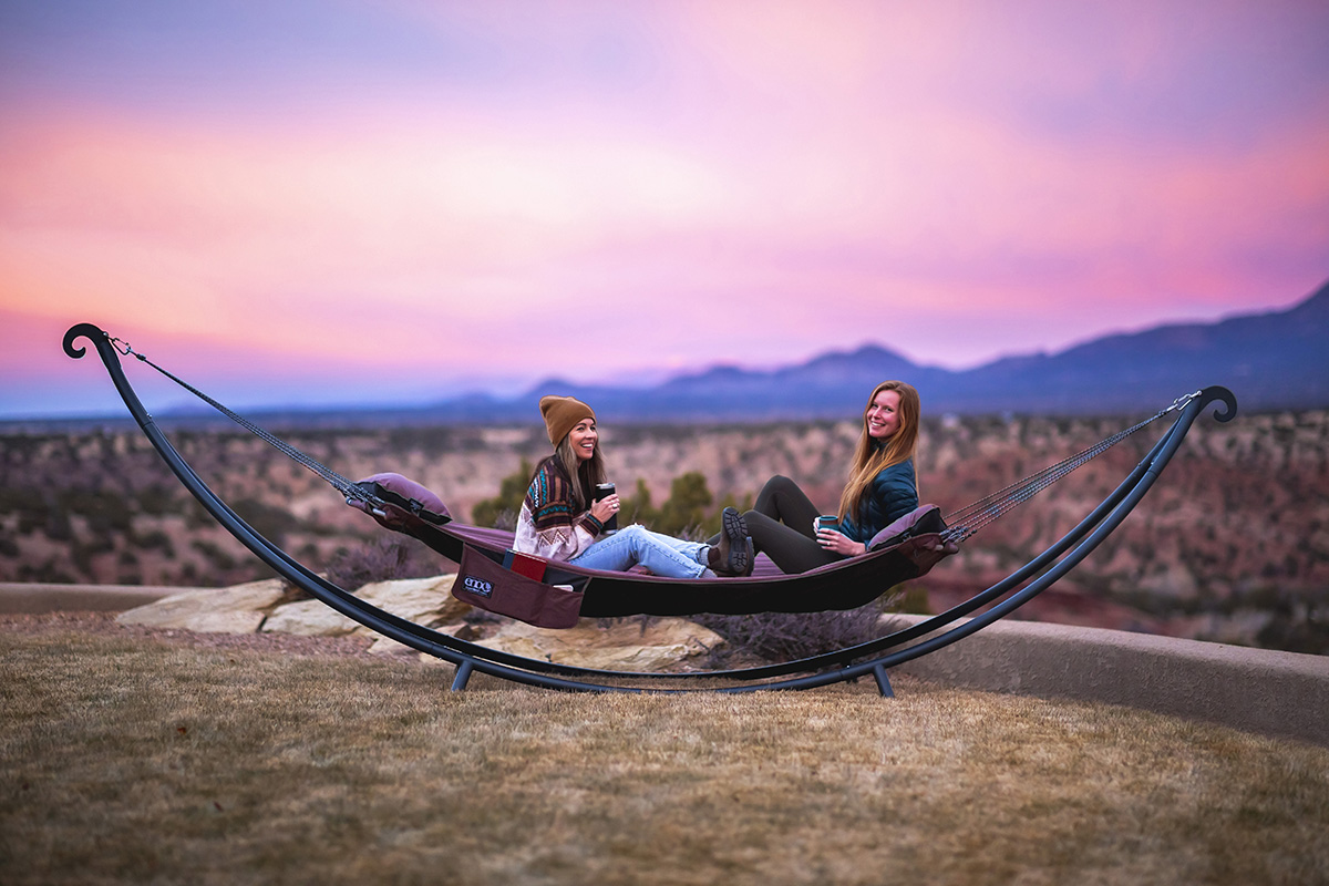 Two women sit in the SuperNest hammock during sunset in New Mexico.