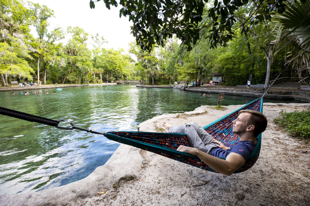 A man lays in an ENO hammock on the edge of Wekiwa Springs State Park.